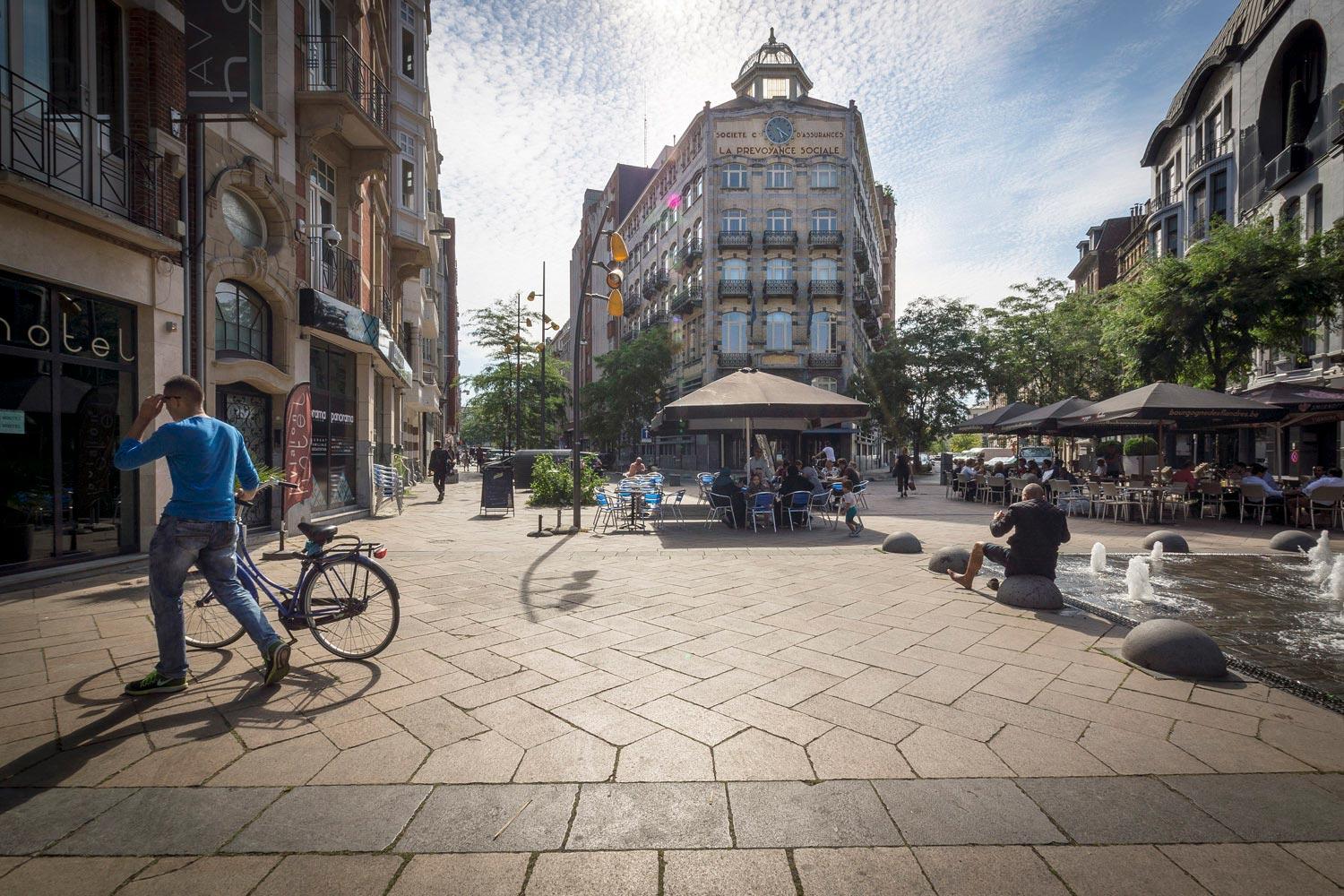 Pedestrian with his bike on Square de l'Aviation, fountain and people sitting